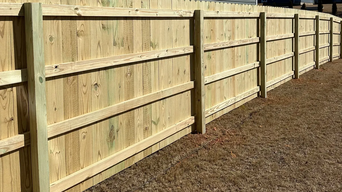 A four board ranch rail fence running away across a wooded lot in long afternoon shadow