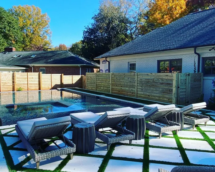 Horizontal slat privacy fence enclosing a pool and turf paver patio behind a white brick home